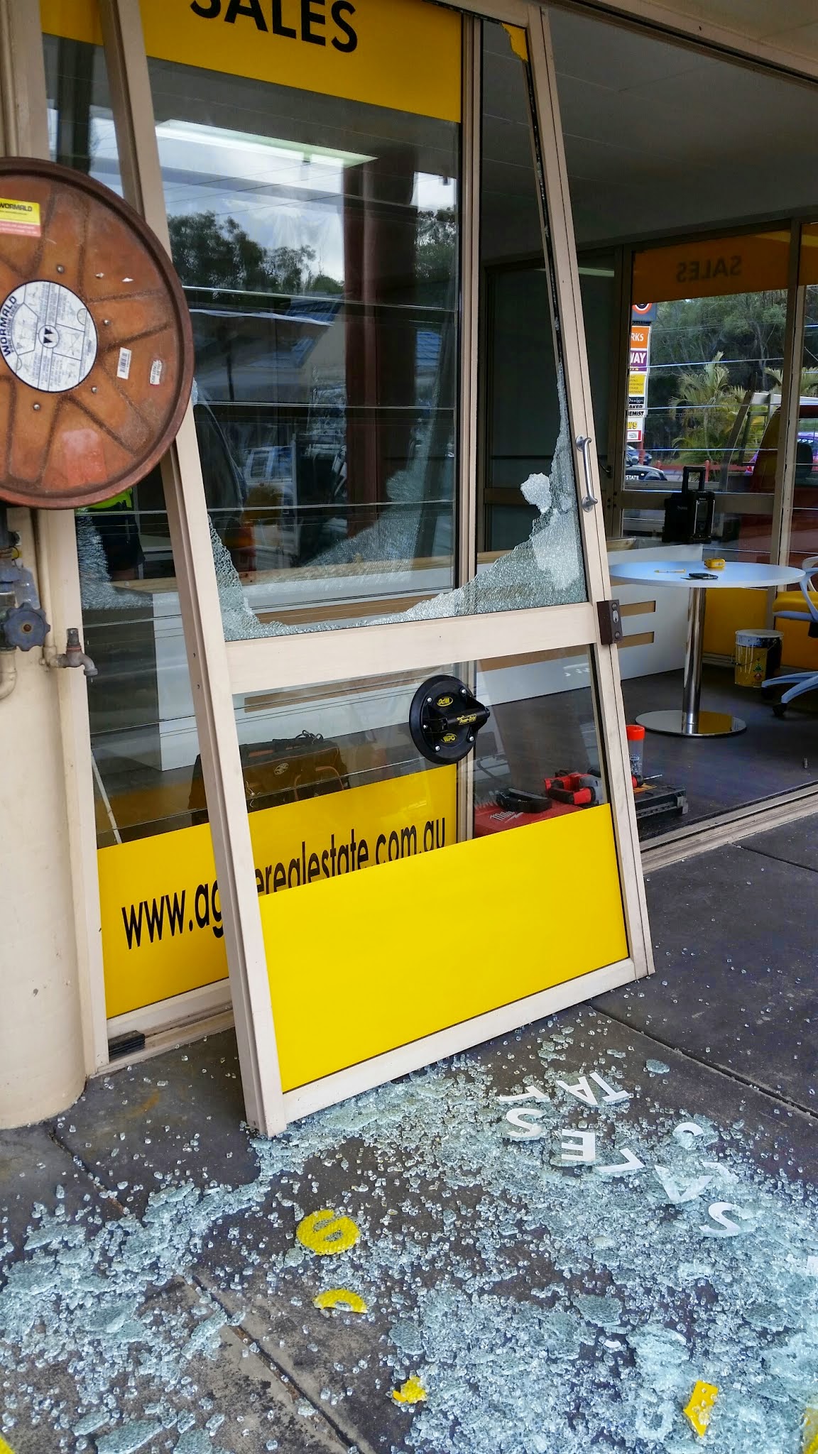 Shattered glass front door at a real estate office, glass on the footpath and Dave's tools inside